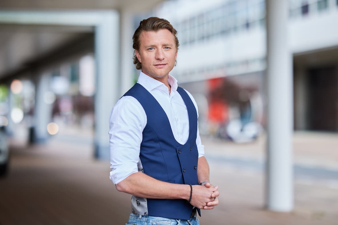 Jan Versteegh buiten poserend voor camera in witte blouse met handen bij elkaar